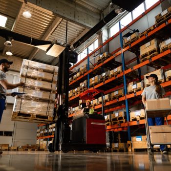 Low angle view of happy warehouse workers communicating while working with shipment in industrial storage compartment.